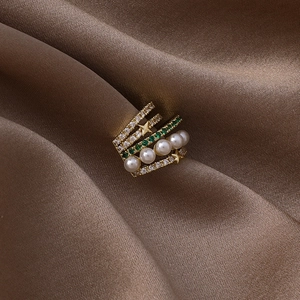 Gros plan sur un earcuff multicouche avec pierres vertes, perles et étoiles dorées