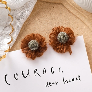 Gros plan de boucles d'oreilles fleurs tricotées marron et gris sur carte blanche