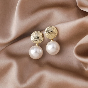 Détail de boucles d'oreilles en métal martelé champagne avec perles blanches élégantes