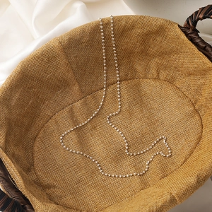 Close-up of golden chain with white mini pearls and beads on a woven background