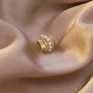 Gros plan d'un ear cuff doré à plusieurs couches avec perles et zircons sur soie champagne