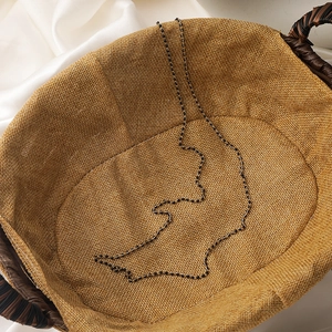 Elegant gold metal chain necklace with small black beads on a woven vintage background