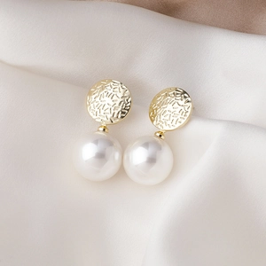 Gros plan de boucles d'oreilles dorées à texture martelée avec grandes perles blanches