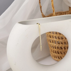 Detail shot of a minimalist gold zircon ear crawler hanging on a ceramic vase rim