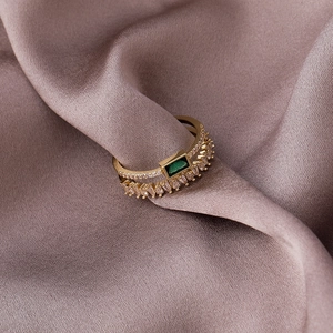 Dettaglio dell'anello in oro a doppio strato con smeraldo verde su raso rosa cipria