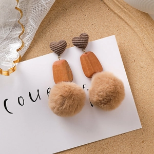 Détail de boucles d'oreilles d'hiver avec cœurs en tricot marron et pompons en peluche