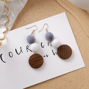 Détail de boucles d'oreilles pompons gris et marron avec pendentif en bois sur carte blanche