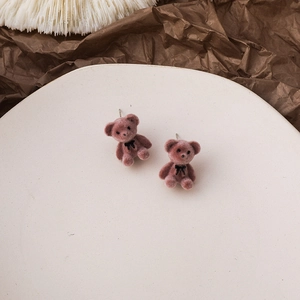 Detail of pink-brown flocked bear earrings with black bow on a white ceramic plate