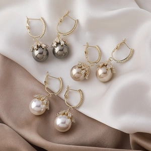 Three pairs of elegant gold pearl drop earrings with sparkling zircon crowns on silk background