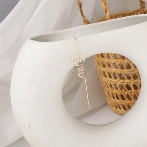 Detail of elegant gold-plated cursive Love letter earring hanging on a white ceramic vase