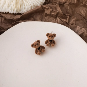 Close-up of cute brown flocked bear earrings with a black bow in a white tray