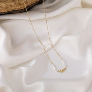 Detail einer eleganten Goldkette mit Perlen und Karabinerverschluss auf weißer Seide