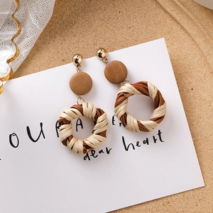 Détail de boucles d'oreilles bohèmes avec disques en bois et pendentifs en rotin tressé
