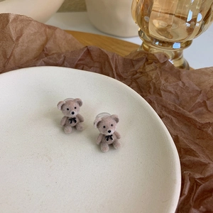 Detail of cute flocking teddy bear earrings with bows on a white ceramic tray