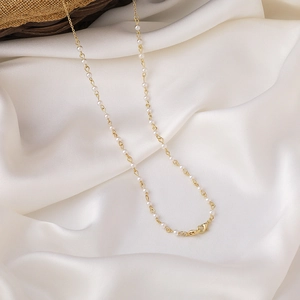 Detail einer eleganten Goldkette mit weißen Perlen auf weißem Seidenhintergrund