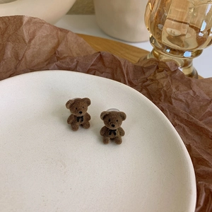 Detailed view of cute brown flocked bear earrings with black bows on a ceramic tray