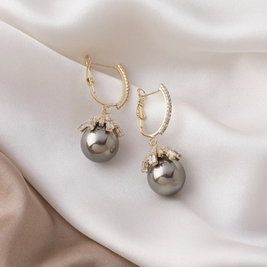 Macro view of gold pearl earrings with sparkling crown settings on silk background