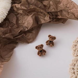 Close-up of brown flocked teddy bear stud earring with a black bow on woven background