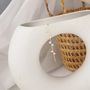 Detail of long gold earring with six clear zircons hanging on white ceramic vase