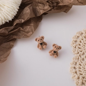 Close-up detail of cute brown flocked teddy bear earrings with black bow decorations