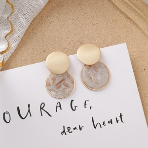 Détail de boucles d'oreilles dorées géométriques avec breloques effet marbre