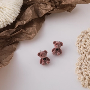 Close-up of pink flocked bear earrings with a black bow on a vintage lace background