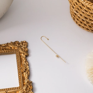 Detail view of gold curved line earrings with clear zircon stones on a decorative background