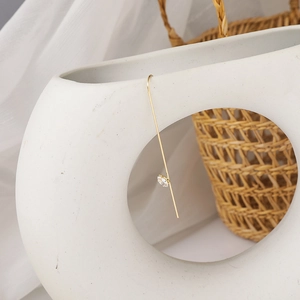 Detail of minimalist gold hook earring with a round crystal zircon on white ceramic vase