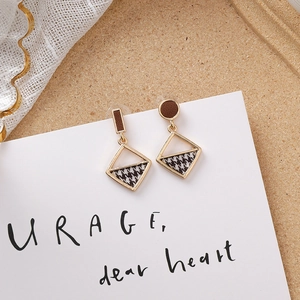 Gros plan de boucles d'oreilles dorées asymétriques avec cuir brun et tissu pied-de-poule