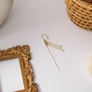Detail of a golden tassel drop ear cuff with fine metal chains on a vintage desk setup