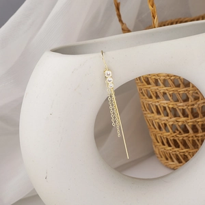 Detail of gold fringe earring with three zircon stones hanging on white ceramic decor