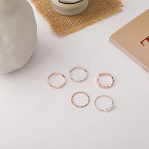 Detail of five rose gold rings including wave bands and pearl accents on warm background