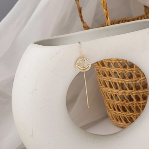 Detail of crystal smiley face earring with gold pendant hanging on a white ceramic vase