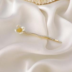 Détail d'une pince à cheveux dorée avec camélia nacré et strass scintillants