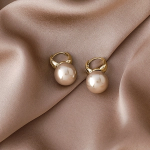 Close-up of elegant gold pearl hoop earrings on champagne silk fabric background