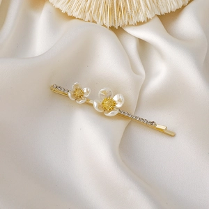 Détail d'une épingle à cheveux dorée avec fleurs de camélia en nacre et strass brillants