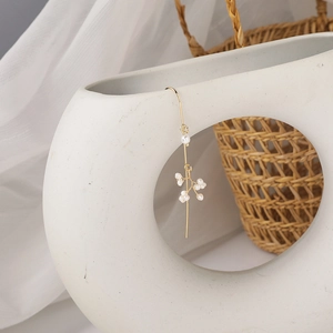 Long gold tassel earrings with cluster pearls draped over a white ceramic vase
