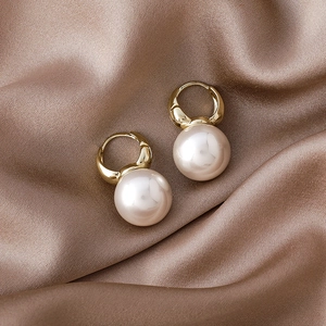 Close-up of elegant gold hoop earrings with large round pearls on champagne silk fabric
