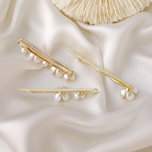 Vue détaillée de trois barrettes à fleurs dorées avec perles sur un tissu de satin blanc