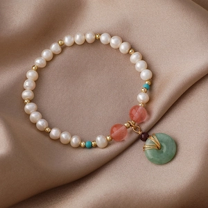 Detail eines Süßwasserperlenarmbands mit grünem Jade-Anhänger auf champagnerfarbener Seide