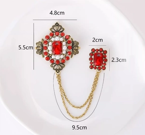 Détail d'une broche vintage avec chaîne vert émeraude et dimensions sur une assiette blanche