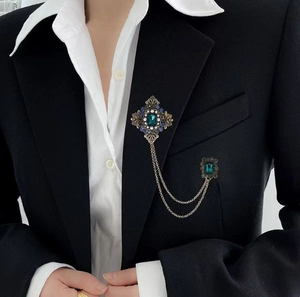 Détail d'une broche vintage avec pierre vert émeraude et chaînes dorées sur veste