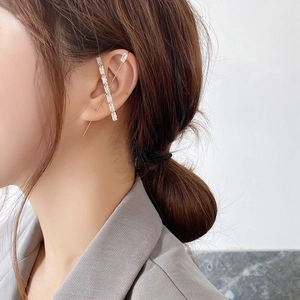 Close-up of a gold cross ear cuff with rectangular crystals on a model ear