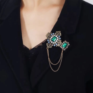 Vue détaillée d'une broche émeraude vintage à pampilles avec strass sur un veston noir