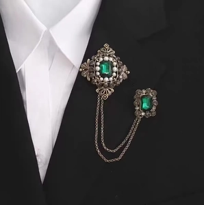 Détail de la broche vintage émeraude avec chaînes dorées sur le revers d'un costume noir