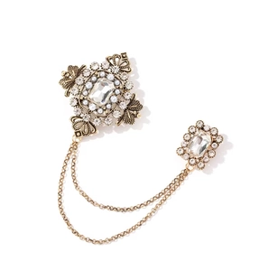 Détail d'une broche vintage émeraude avec chaînes dorées et accents de perles