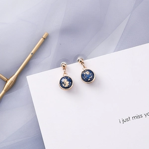 Detail of round starburst earrings in blue resin with gold flakes and golden studs