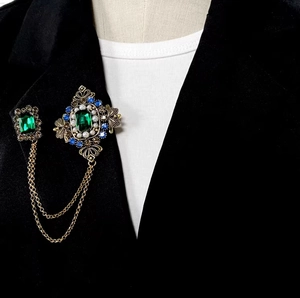 Détail d'une broche vintage avec émeraude et chaînes dorées sur un blazer noir élégant