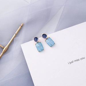 Detail of blue geometric earrings featuring oval and rectangular dangles with glitter texture