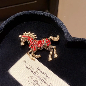 Macro shot of retro horse brooch with red crystals and gold texture on black velvet